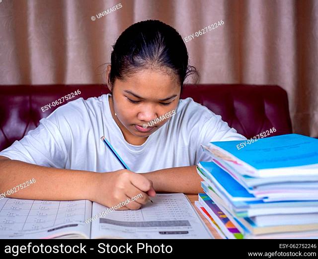 girl doing homework on a wooden table and there was a pile of books next to it The background is a red sofa and cream curtains