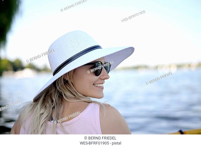 Smiling young woman wearing sunglasses and white summer hat al lake