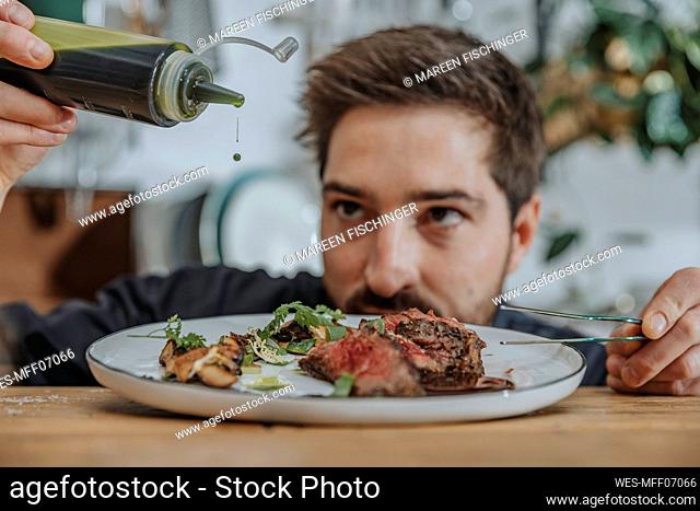 Expertise adding sauce over cooked tomahawk steak in plate while working in kitchen