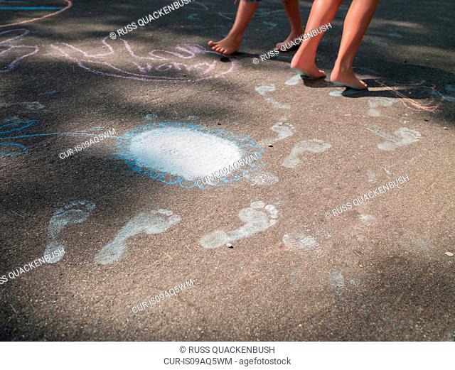 Bare feet of two sisters making chalk footprints on pavement