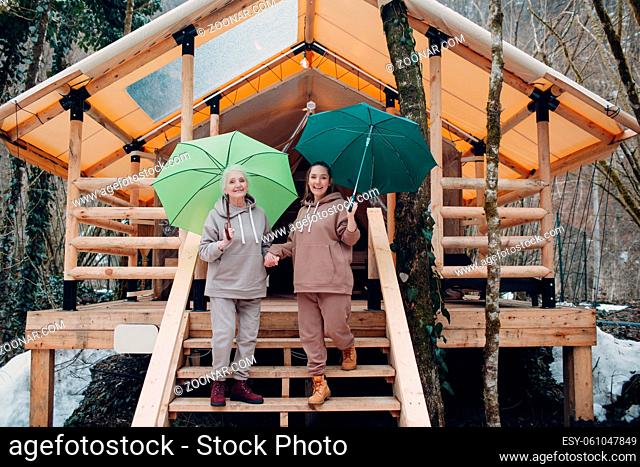 Elderly and young adult woman with umbrella at glamping camping tent. Modern vacation lifestyle concept