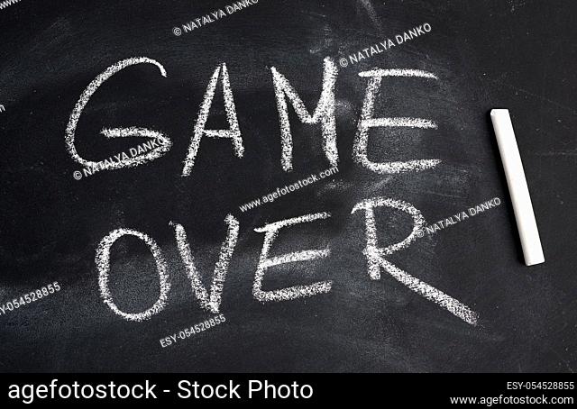 inscription in English game over with white chalk on a black board, concept of ending the process