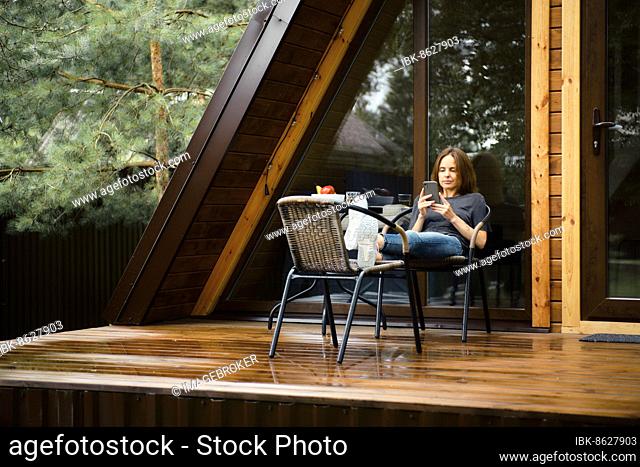 Cute woman with smartphone on terrace of her a-frame cabin