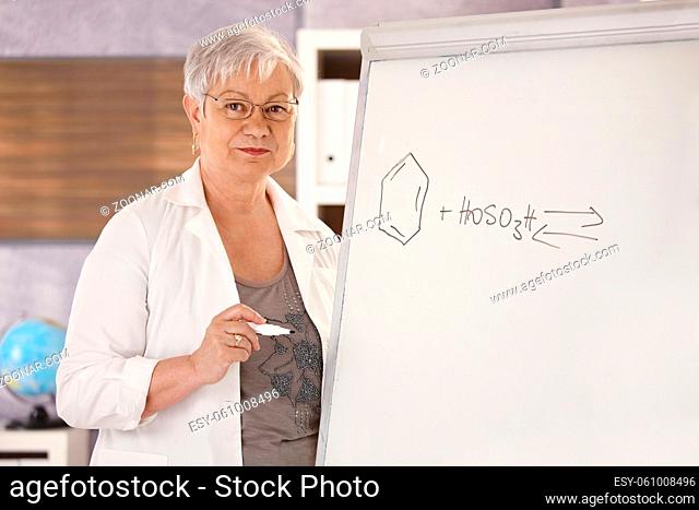Senior teaching chemistry in school, drawing molecular formulas on whiteboard