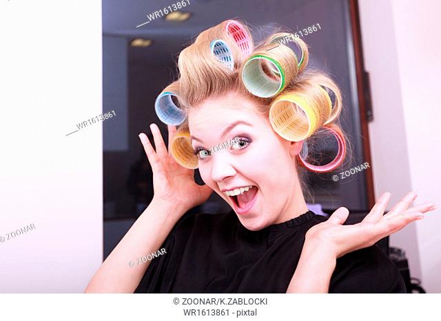 Cheerful funny blond girl hair curlers rollers by haidresser in beauty salon