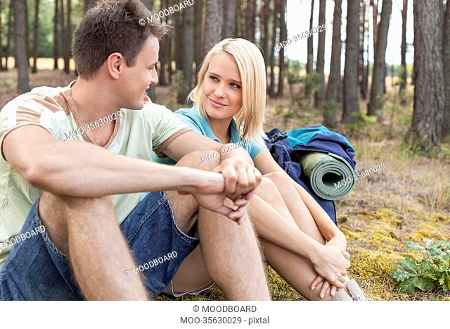 Hiking couple looking at each other while relaxing in forest