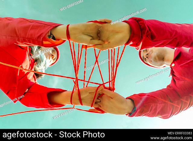 Crop view of young couple dressed in red performing with red string against sky
