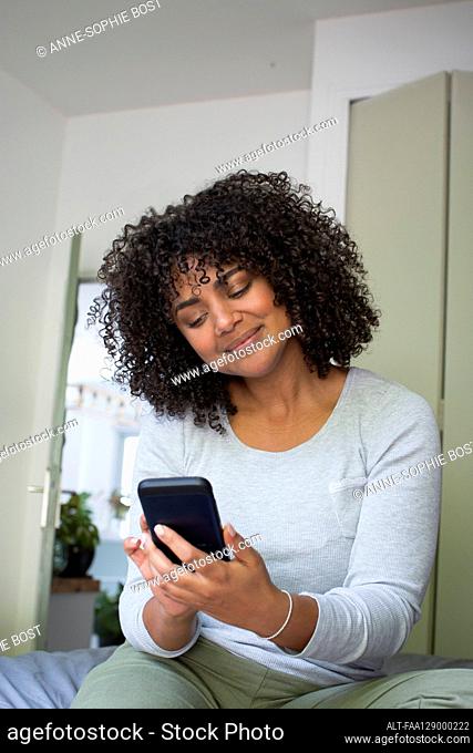 Woman using smart phone while sitting in bedroom