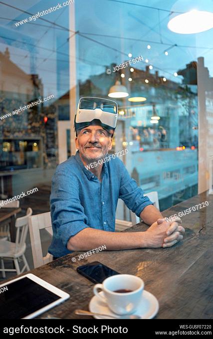 Businessman with virtual reality simulator sitting at table by window in cafe
