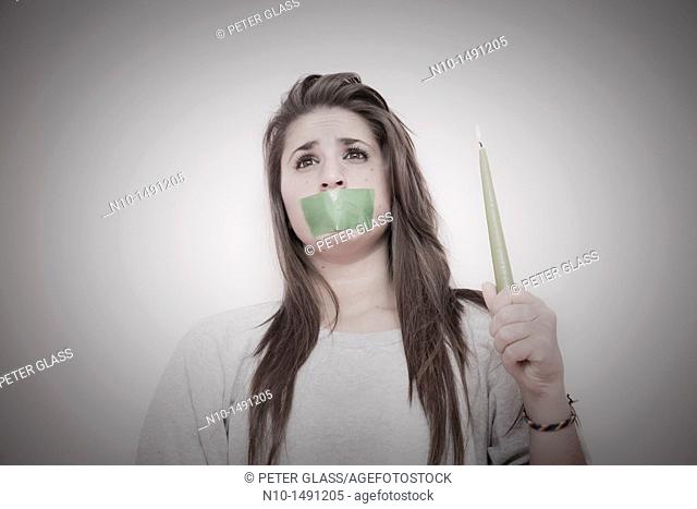 Teen girl with tape over her mouth, holding a lit candle