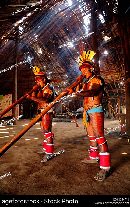 Two indios playing their long pipe inside a hut while the rays of the sun are vidible, Mato Grosso, Brazil, South America