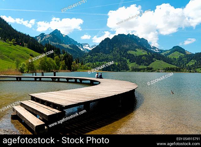 Schwarzsee, FR / Switzerland - 1 June 2019: two men best friends enjoy the summer lakeside view at the Schwarzsee Lake in the Swiss Alps in canton Fribourg