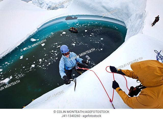 Guide lowers climbers to base of iceberg , ice climbing on grounded iceberg, Cruise ship passengers look on, Pleneau Island, Antarctic Peninsula
