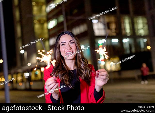 Happy woman with sparklers standing on street at night
