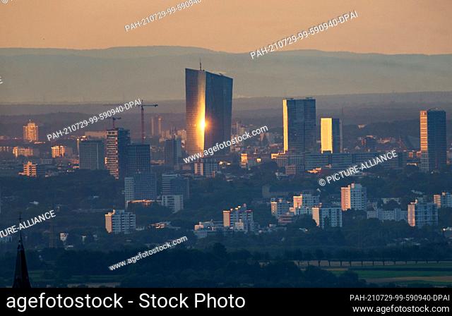 29 July 2021, Hessen, Kronberg: The light of the rising sun is reflected by the skyscraper of the European Central Bank (ECB) headquarters as you look down on...