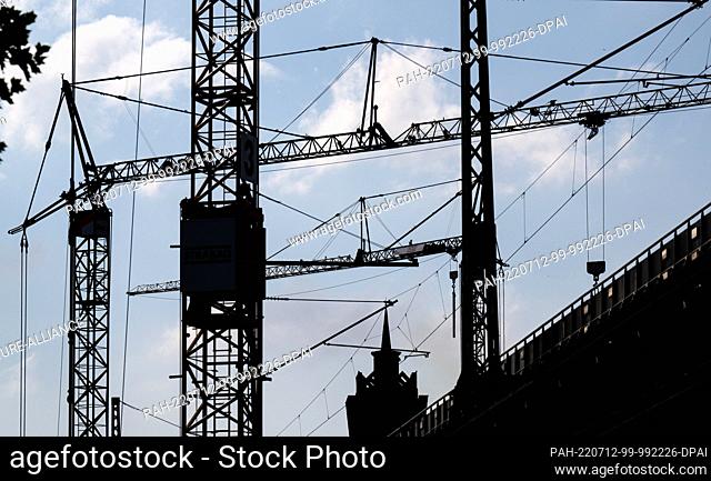 12 July 2022, Saxony, Chemnitz: Backlit behind the construction site of the historic railroad viaduct in Chemnitz is the silhouette of the distinctive Wirkbau...