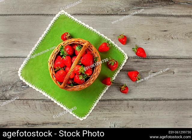 Tabletop view, small basket full of strawberries, some of them spilled on green table cloth under it