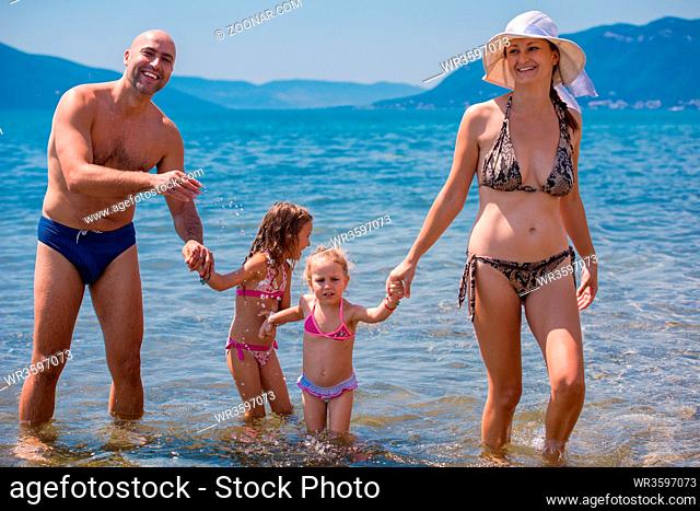 portrait of a young happy couple with cute little daughters having fun while standing in the shallow water of the sea during Summer vacation Healthy family...