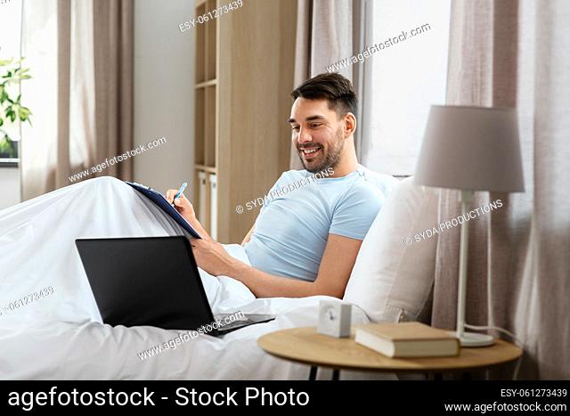 man with laptop working in bed at home bedroom