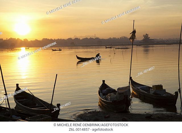 sunrise over the lake with fishermen on boats fishing in the lake near wooden foot bridge U Bein Bridge crossing the Taungthaman Lake near Amarapura in Mandalay...
