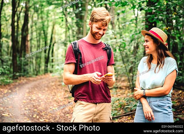 Hikers using mobile gps for directions. Happy couple checking smartphone in the woods during backpacking trip. Young joyful couple using gps map