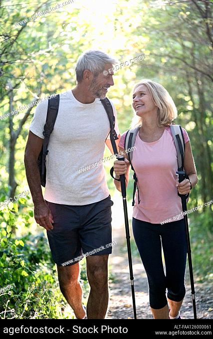 Smiling mature couple looking at each other while hiking in forest