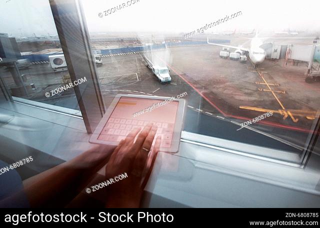Close-up shot of woman using touch pad while waiting for the flight. Airport area in background. Blur motion with zooming out effect