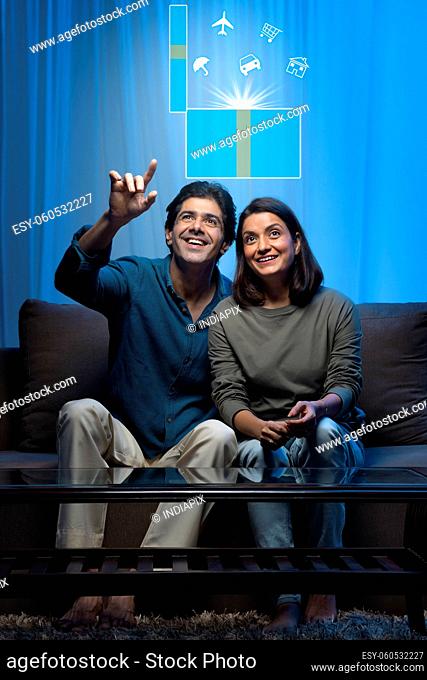 Indian middle age married couple dreaming about future while sitting on sofa