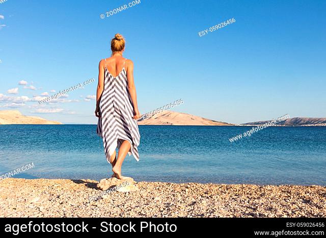 Happy carefree woman enjoying late afternoon walk on white pabbled beach on Pag island, Croatia