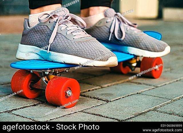 Picture of a girl's legs wearing old sneakers which stands on a blue skateboard on a pavement, selective focus and vintage toning. Grownd level shot