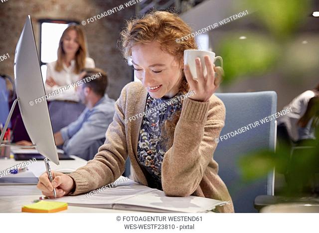 Young woman working in modern creative office, holding cup of coffee