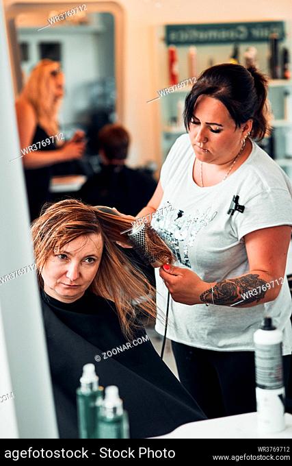 Hairdresser styling dyeing combing womans hair. Young woman working as a hairdresser in hair salon. Real people, authentic situations