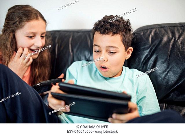 Little boy and his sister are playing on handheld game consoles at home
