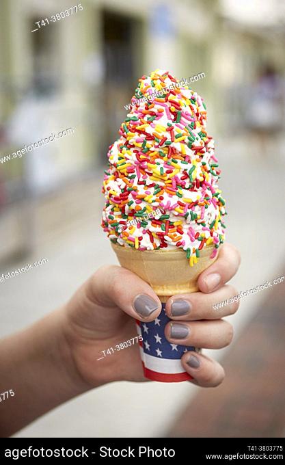 A young girl's hand holding a melting ice cream cone with sprinkles