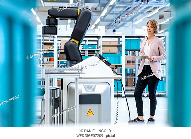 Businesswoman with tablet in a modern factory hall looking at robot