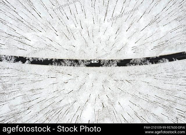 dpatop - 09 January 2021, North Rhine-Westphalia, Winterberg: A car drives across a road through a snow-covered forest (aerial photo with drone)