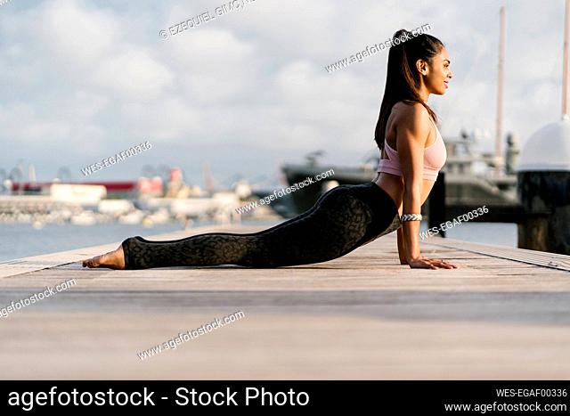 Athlete practicing upward facing dog pose on pier at harbor
