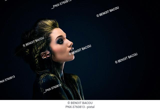 Portrait of a young woman in profile, the body painted black and gold, the look on the side