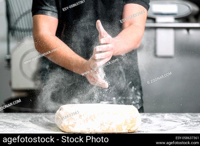 Baker claping hands with flour in restaurant kitchen
