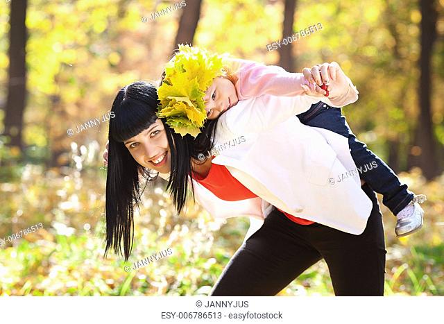 beautiful young mother holding her daughter in a wreath of maple leaves on back