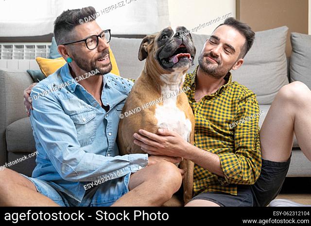 Happy gay couple sitting on floor and playing with dog at home. High quality photography