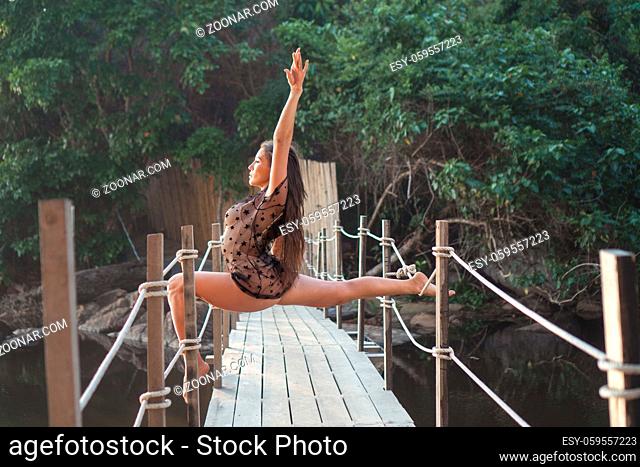 Beautiful acrobat woman posing on the ropes of the small wooden bridge during summer day
