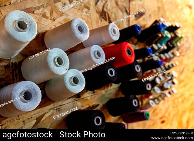 Various colors and grades of thread spools are viewed close-up, hung on an OSB wall for easy access and organization, inside a fashion workshop