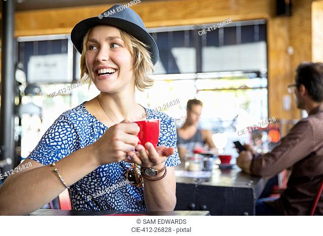 Smiling woman drinking coffee looking over shoulder in cafe