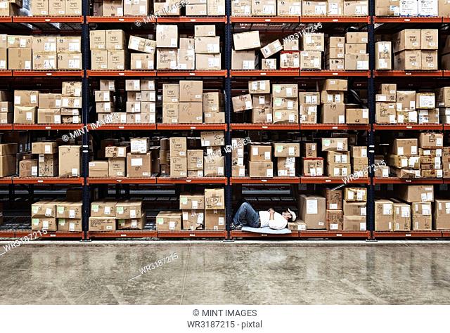 Warehouse worker taking a break next to large racks of cardboard boxes holding product in a distribution warehouse