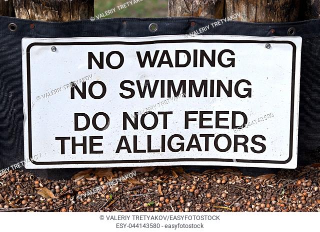 White warning sign with black letters. No Wading. No Swimming. Do not feed the Alligators. Seen in Florida