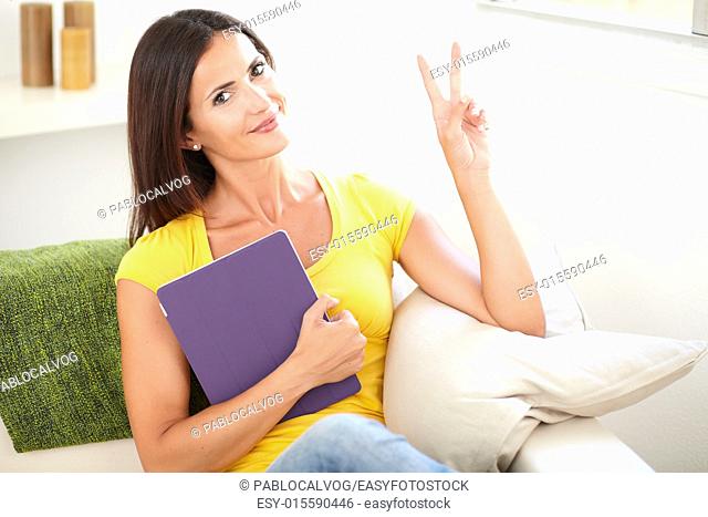 Relaxed woman in yellow shirt making a victory sign while holding a tablet