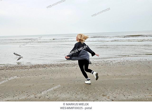 Netherlands, happy blond young woman running on the beach