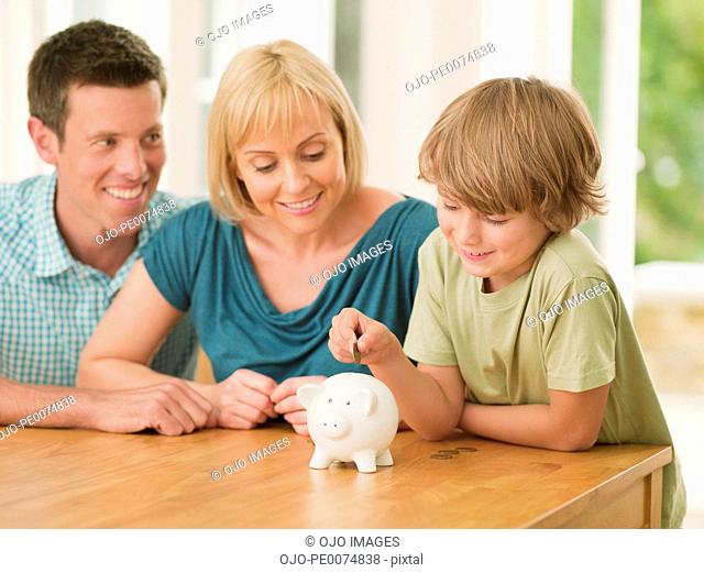 Parents watching son putting coin into piggy bank