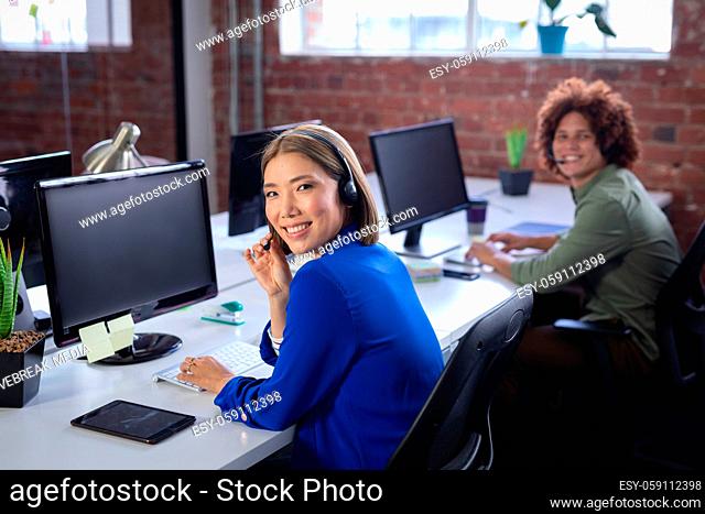 Happy diverse male and female colleagues sitting in front of computers wearing headsets